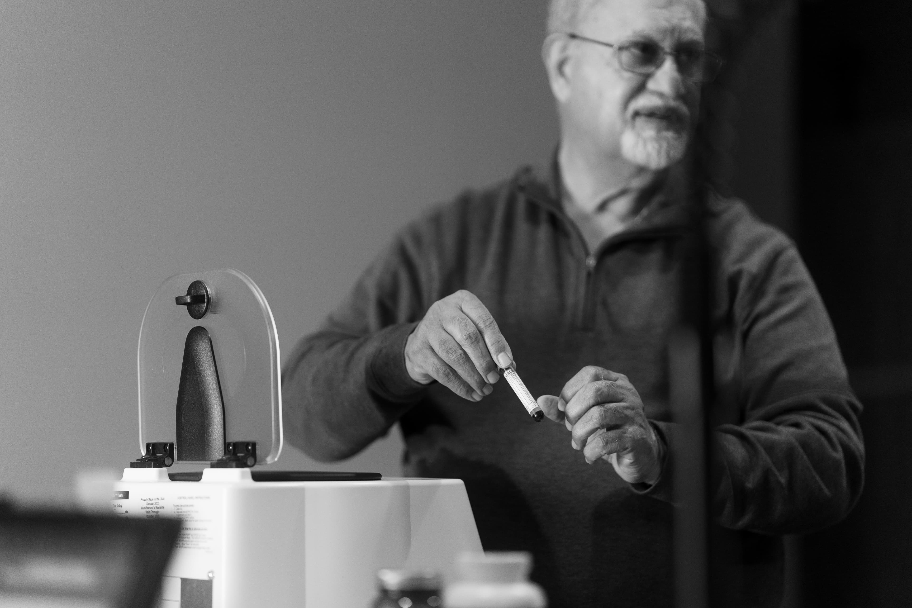 Dr. Khanna retrieving the blood sample from the centrifuge and explaining to the pet's owner how the test will work. Photo in black and white.