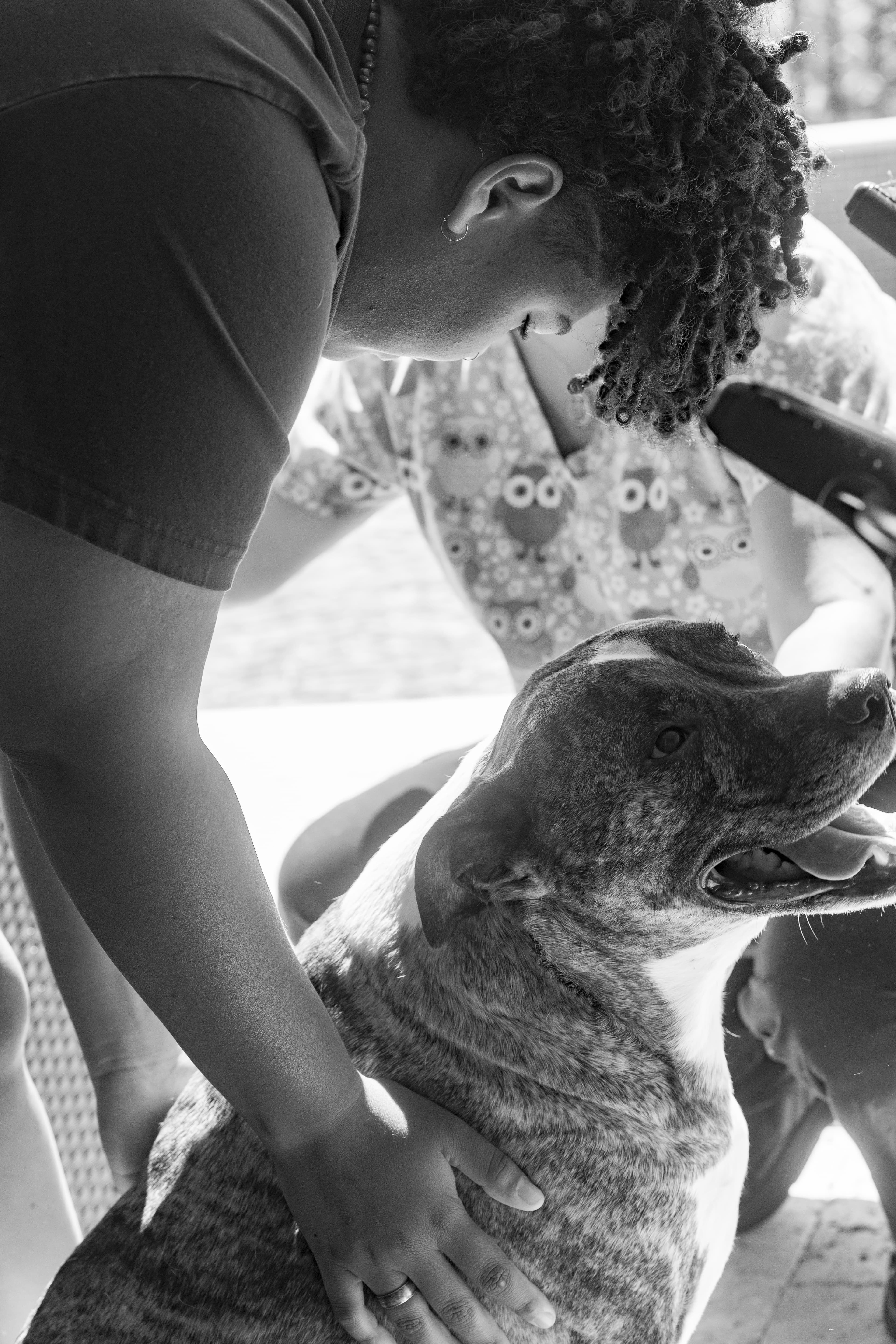 Gia inspecting the skin of the puppy, while the owner pets the puppy. The puppy has its head turned towards the camera and is panting. Photo in black and white.