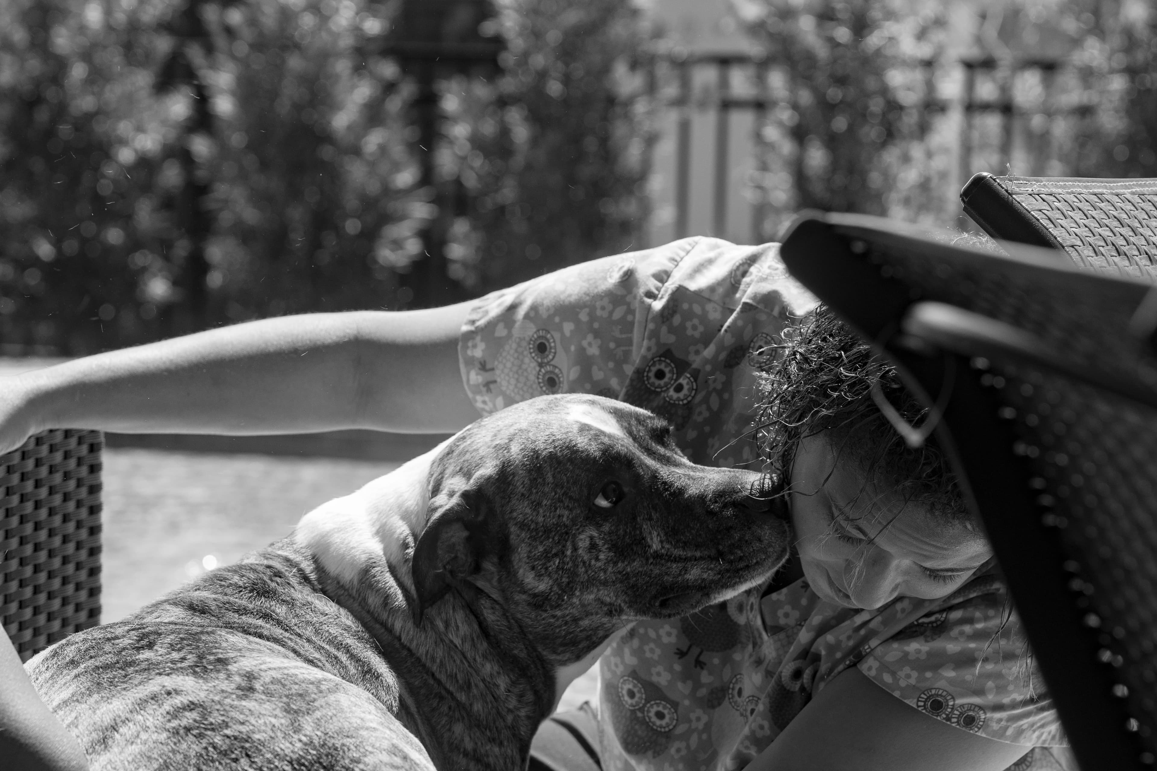 Gia squatting to look at a puppy, while the puppy inspects Gia with his nose inquisitively. Photo in black and white.